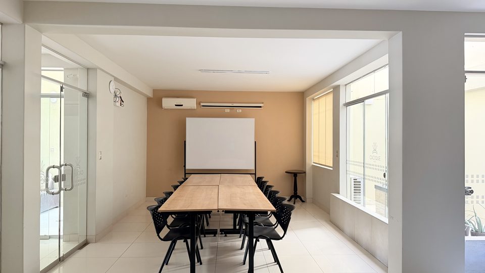Auditorio del Cacique Hotel con mesa de trabajo para 14 personas y ecran de proyección
