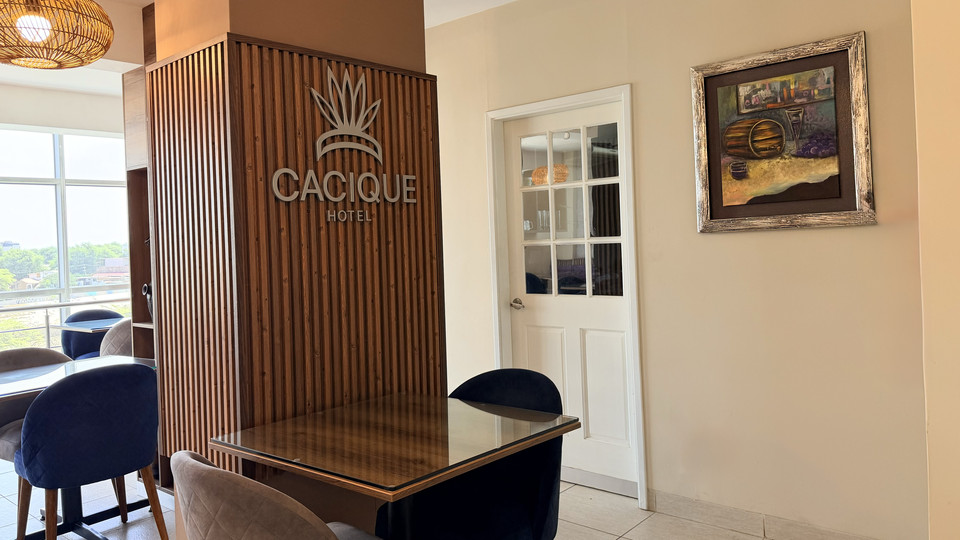 Mesas del restaurante del Cacique Hotel junto al panel de madera con el logotipo
